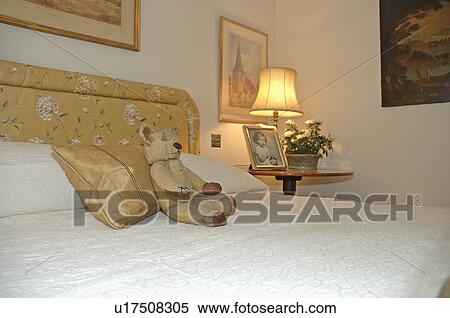 Lighted lamp on table in corner of small bedroom with teddy-bear and white bedlinen on upholstered bed View Large Photo Image Stock Photography - Lighted lamp on table in corner of small bedroom with teddy-bear and white bedlinen on upholstered bed. Fotosearch