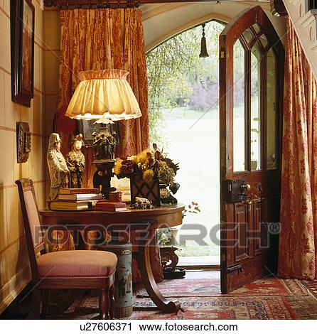 Lighted lamp on table in country hall with Gothic-style door open to view of garden View Large Photo Image Stock Image - Lighted lamp on table in country hall with Gothic-style door open to view of garden. Fotosearch