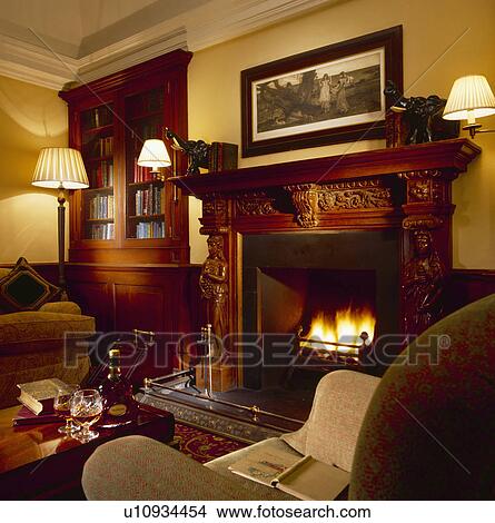 Lighted lamps in cosy living room with fire lit in fireplace View Large Photo Image Picture - Lighted lamps in cosy living room with fire lit in fireplace. Fotosearch