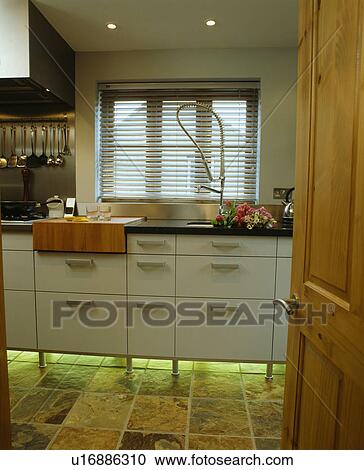 Stock Image - Lighting below fitted unit in modern white kitchen. Fotosearch