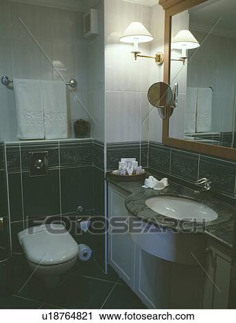 Stock Image - Lighting beside mirror above undermounted basin in modern bathroom . Fotosearch