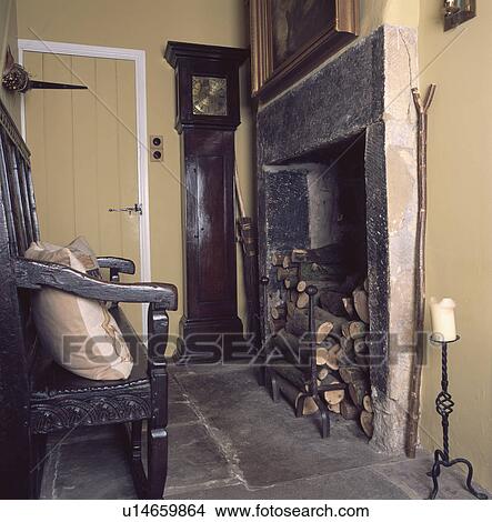 Logs in stone fireplace of small living room with oak settle and longcase clock View Large Photo Image Picture - Logs in stone fireplace of small living room with oak settle and longcase clock. Fotosearch