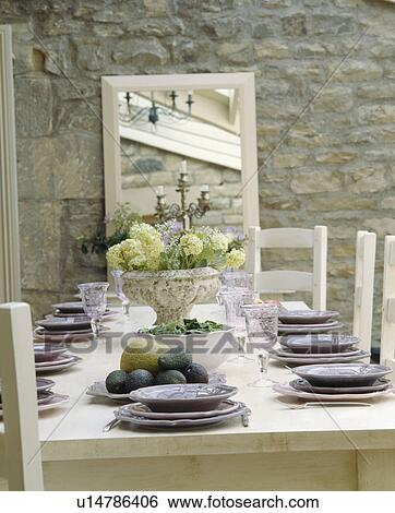 Stock Photograph - mauve plates on table set for lunch in dining room with mirror on stone wall. Fotosearch