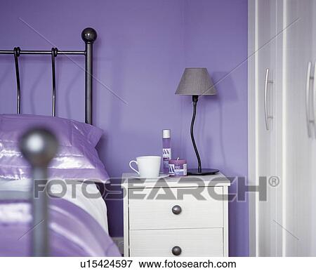 Stock Photo - Metal lamp on white bedside table beside metal bed in mauve bedroom. Fotosearch