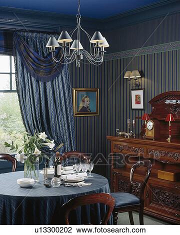 Metal light above table with blue cloth in dining room with blue swagged curtains and blue striped wallpaper View Large Photo Image Stock Image - Metal light above table with blue cloth in dining room with blue swagged curtains and blue striped wallpaper. Fotosearch