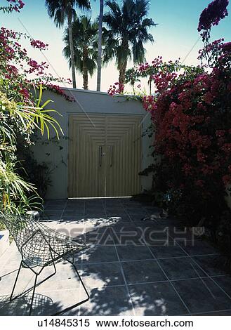 Metal mesh chair on slate paving in walled garden with double wooden gates View Large Photo Image Stock Photography - Metal mesh chair on slate paving in walled garden with double wooden gates . Fotosearch