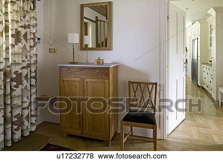 Mirror above small wooden cupboard and antique chair beside patterned curtains at window in country hall View Large Photo Image Stock Photo - Mirror above small wooden cupboard and antique chair beside patterned curtains at window in country hall. Fotosearch