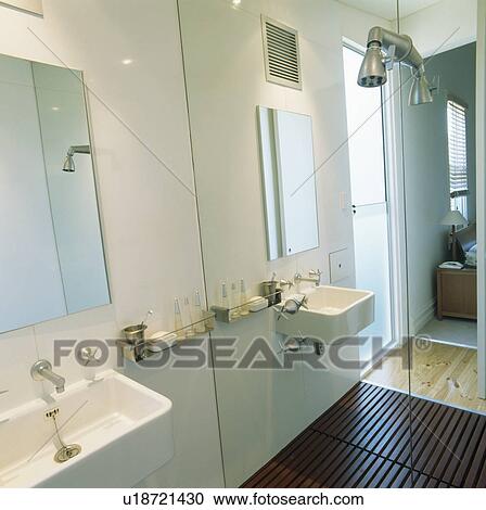 Stock Image - Mirrored wall in modern white bathroom with white sink and wooden flooring. Fotosearch