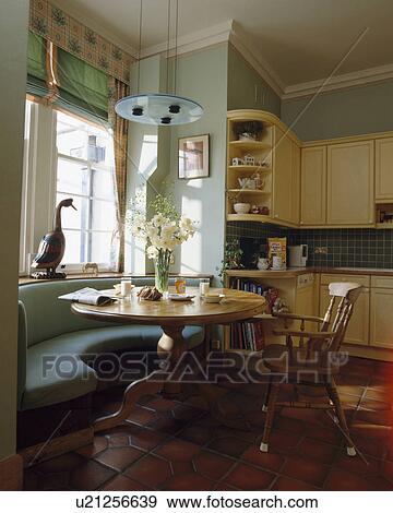 Modern disc-light above circular pine table and curved window-seat in pastel green and cream kitchen View Large Photo Image Stock Photo - Modern disc-light above circular pine table and curved window-seat in pastel green and cream kitchen. Fotosearch