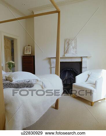 Modern four-poster bed in white bedroom with white armchair beside fireplace View Large Photo Image Stock Photo - Modern four-poster bed in white bedroom with white armchair beside fireplace. Fotosearch