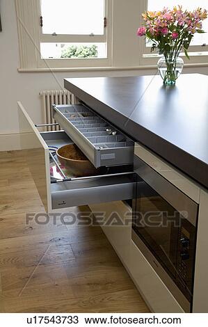 Stock Image - Modern kitchen with open storage drawers on island unit with cast concrete resin worktop. Fotosearch