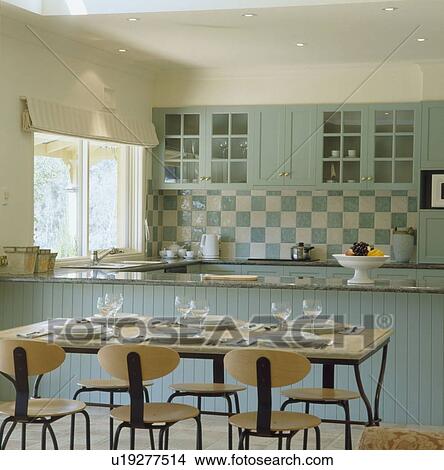 Modern plywood and metal table and chairs in kitchen with pale turquoise fitted units and turquoise and cream wall tiles View Large Photo Image Picture - Modern plywood and metal table and chairs in kitchen with pale turquoise fitted units and turquoise and cream wall tiles. Fotosearch