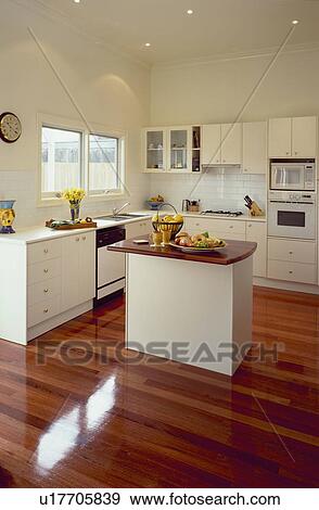 Stock Photo - Modern white kitchen with island unit and wooden flooring. Fotosearch