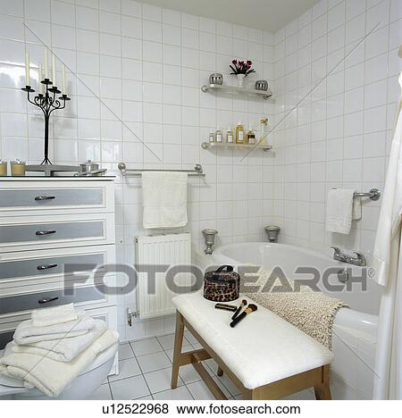 Modern white tiled bathroom with small chest-of-drawers and upholstered stool View Large Photo Image Stock Photo - Modern white tiled bathroom with small chest-of-drawers and upholstered stool. Fotosearch