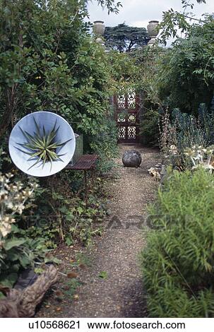 Stock Image - Novelty disc sculpture beside gravel path in country garden. Fotosearch