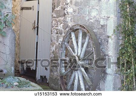 Stock Image - Old cartwheel against stone wall with dilapidated door. Fotosearch