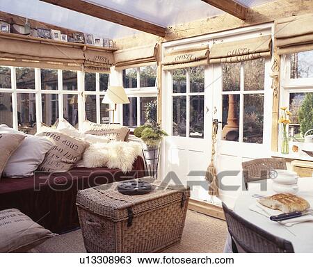 Stock Image - Old wicker chest in conservatory with blinds and cushions made from hessian sacks. Fotosearch