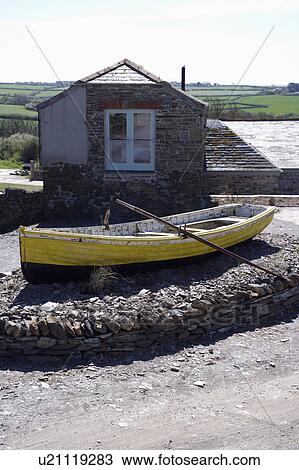 Stock Image - Old wooden rowing-boat in front of coastal cottage. Fotosearch