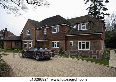 Open-top car on gravel drive in front of large traditional brick-built house View Large Photo Image Picture - Open-top car on gravel drive in front of large traditional brick-built house. Fotosearch