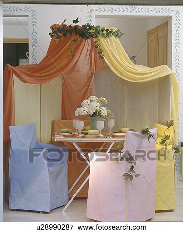 Orange and yellow voile drapes above table and director's chairs with blue, pink and yellow pastel loosecovers View Large Photo Image Stock Photo - Orange and yellow voile drapes above table and director's chairs with blue, pink and yellow pastel loosecovers. Fotosearch