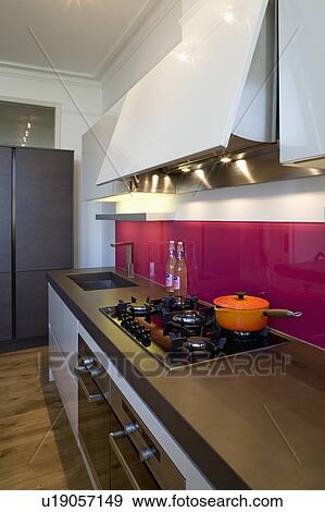 Stock Photo - Orange pan on hob in modern kitchen with red glass splashbacks and cast concrete resin worktop. Fotosearch