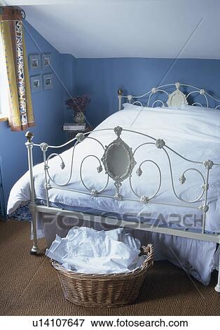 Stock Photo - Ornate antique white cast-iron bed in blue attic bedroom with white linen stored in basket at the foot of the bed. Fotosearch