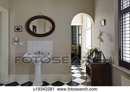 Stock Image - Oval mirror above white pedestal basin in beige traditional bathroom. Fotosearch