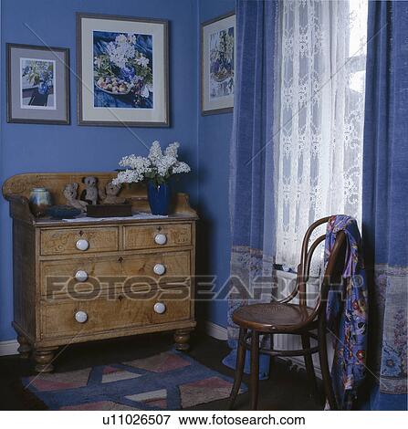 Stock Photo - Painted chest of drawers and bentwood chairin blue bedroom with blue curtains. Fotosearch