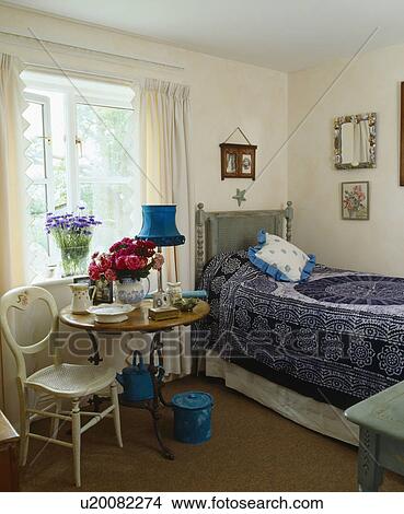 Painted Victorian chair and small circular table in front of window in cottage bedroom with blue bedline on single bed View Large Photo Image Picture - Painted Victorian chair and small circular table in front of window in cottage bedroom with blue bedline on single bed. Fotosearch