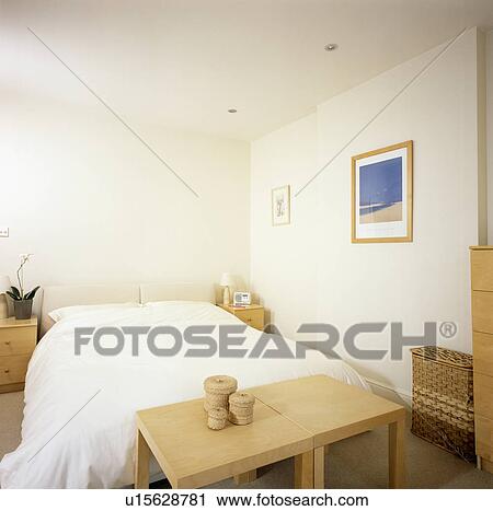 Pair of simple pale wood tables below bed with white bedlinen in economy-style bedroom View Large Photo Image Stock Image - Pair of simple pale wood tables below bed with white bedlinen in economy-style bedroom. Fotosearch