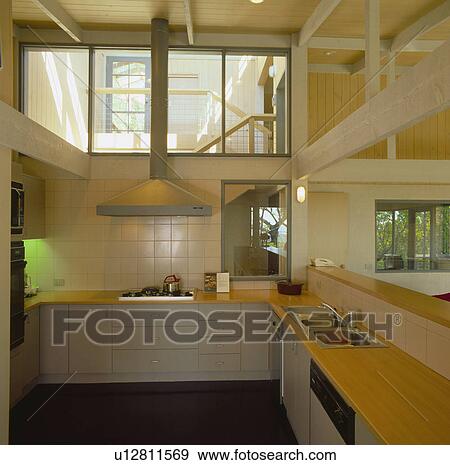Stock Photo - Pale grey fitted units in modern kitchen with internal windows onto staircase. Fotosearch
