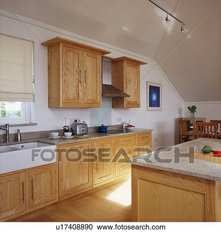 Stock Image - Pale wood fitted units in modern white kitchen. Fotosearch