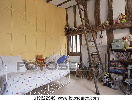 Panelled yellow wall above white iron bed in child's bedroom with wooden ladder View Large Photo Image Stock Photo - Panelled yellow wall above white iron bed in child's bedroom with wooden ladder. Fotosearch