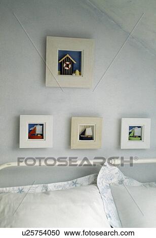 Stock Image - Pastel blue bedroom with small pictures above bed. Fotosearch