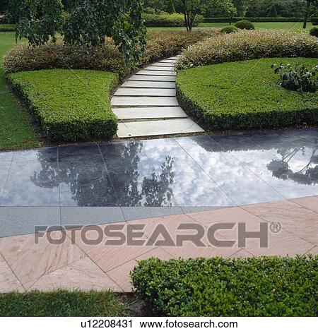 Stock Image - Path through low clipped box to terrace with contrasting polished slate and stone paving. Fotosearch