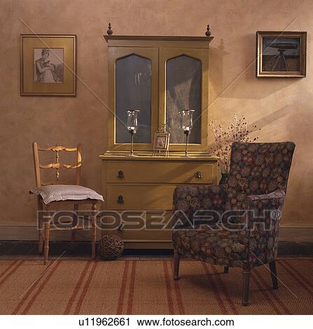 Stock Image - Patterned blue armchair and pastel green cupboard in cottage living room. Fotosearch