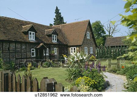 Stock Image - Paved path through small lawns and borders with summer flowering plants to country cottage. Fotosearch