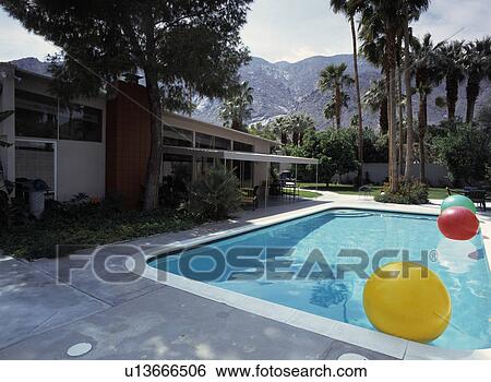 Paving around turquoise swimmingpool in garden with palm trees in front of modern house with backdrop of mountains View Large Photo Image Stock Photograph - Paving around turquoise swimmingpool in garden with palm trees in front of modern house with backdrop of mountains. Fotosearch