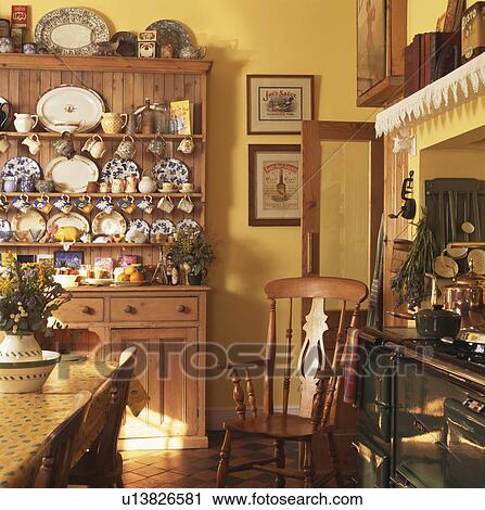 Stock Image - Pine dresser and Windsor chair in yellow country kitchen. Fotosearch
