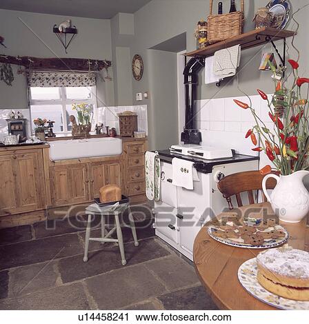 Stock Image - Pine table and white Aga oven in grey country kitchen with fitted pine units and slate tiled floor. Fotosearch