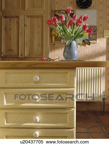 Stock Photography - Pink tulips in vase on kitchen unit with cream drawers. Fotosearch