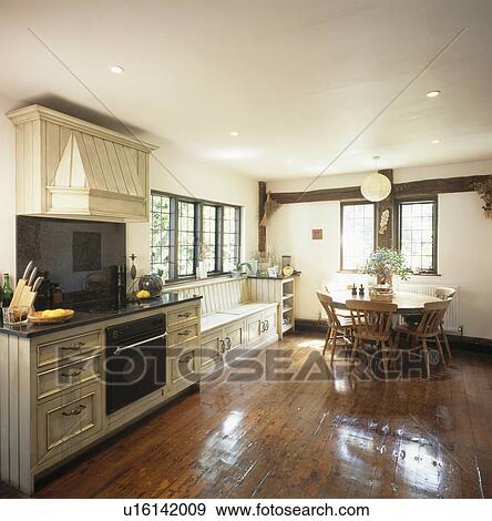 Stock Photo - Polished wooden floorboards in large cream country kitchen with wooden table and chairs. Fotosearch
