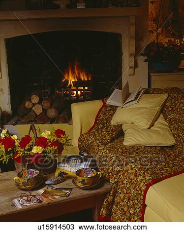 Stock Image - Quilted throw on yellow sofa in front of fireplace in cosy living room. Fotosearch