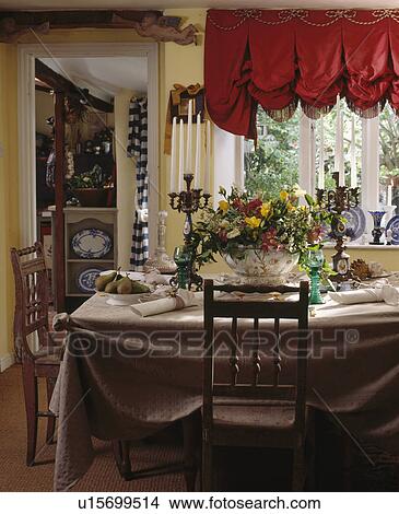 REd festoon blind on window in small cottage dining room with fresh flower arrangement on table with beige cloth View Large Photo Image Picture - REd festoon blind on window in small cottage dining room with fresh flower arrangement on table with beige cloth. Fotosearch