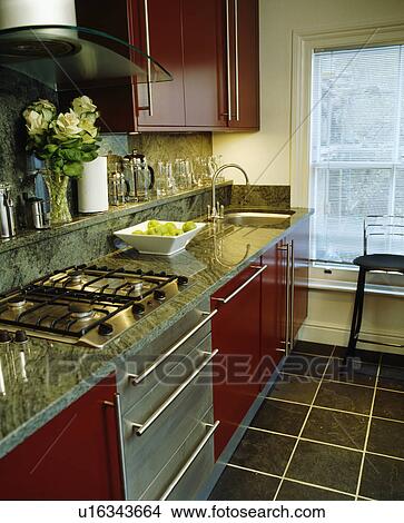 Picture - Red fitted units in modern kitchen with hob in grey granite worktop. Fotosearch
