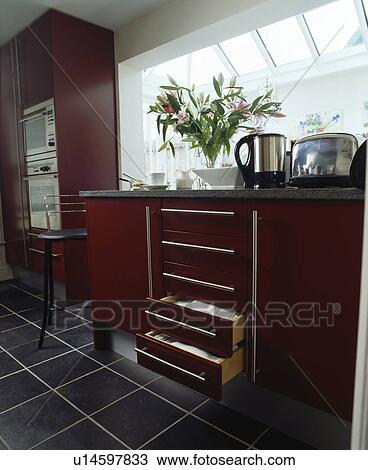 Stock Image - Red fitted units in modern townhouse kitchen with slate flooring. Fotosearch