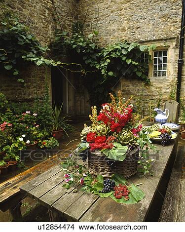 Picture - Red roses in informal flower arrangement in basket on old wooden table in courtyard of traditional country house. Fotosearch