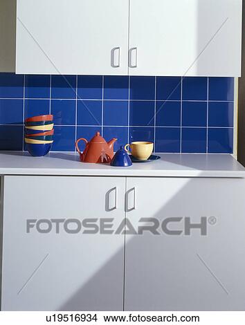 Red teapot on worktop below blue wall tiles and white kitchen cupboard View Large Photo Image Picture - Red teapot on worktop below blue wall tiles and white kitchen cupboard. Fotosearch