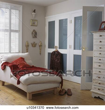 Stock Image - Red throw on white chaiselongue in bedroom with blue+white fittede wardrobe. Fotosearch