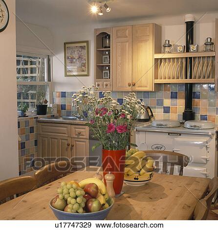 Red vase of flowers and bowls of fruit on pine table in country kitchen with cream Aga oven View Large Photo Image Stock Photo - Red vase of flowers and bowls of fruit on pine table in country kitchen with cream Aga oven. Fotosearch